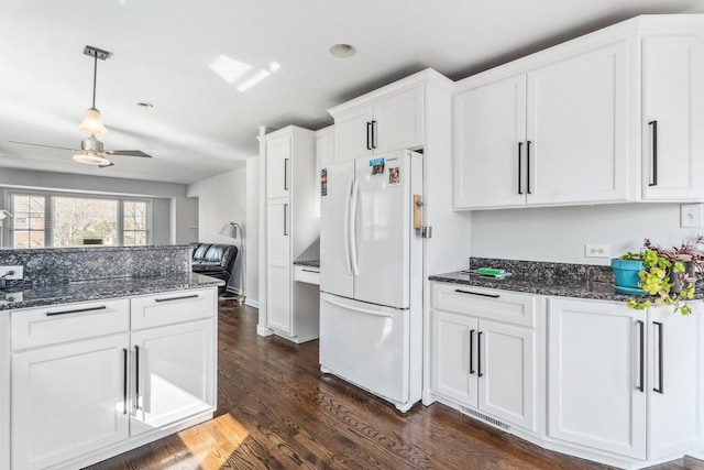 kitchen featuring white cabinets, dark stone counters, freestanding refrigerator, and dark wood-type flooring