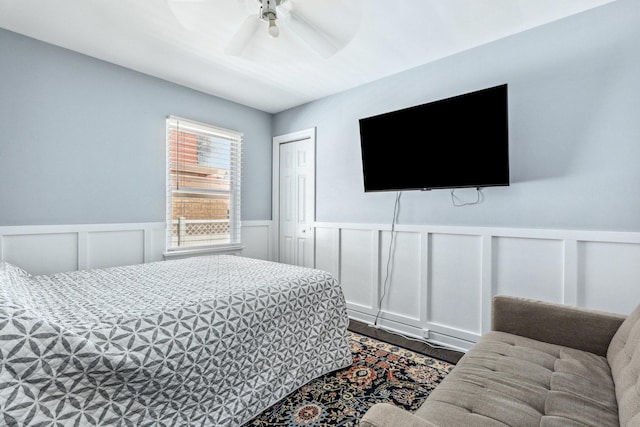 bedroom with a wainscoted wall, a closet, a ceiling fan, and a decorative wall