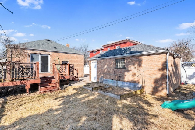 back of house with brick siding, a wooden deck, roof with shingles, and a garden