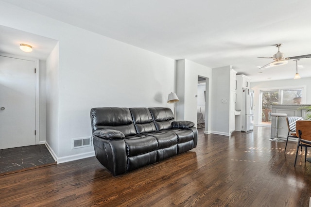 living area with visible vents, baseboards, dark wood-type flooring, and ceiling fan