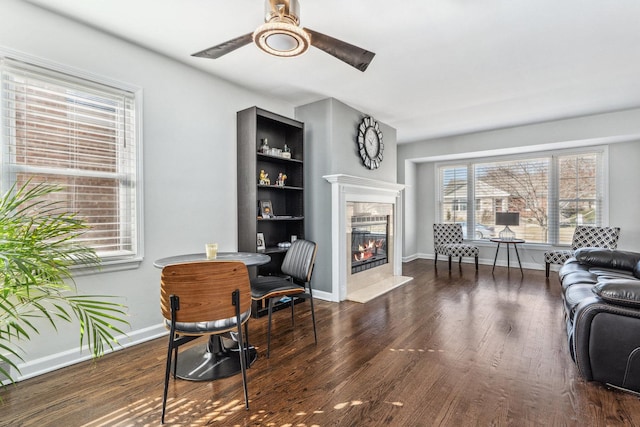 living room featuring a tiled fireplace, a ceiling fan, baseboards, and wood finished floors