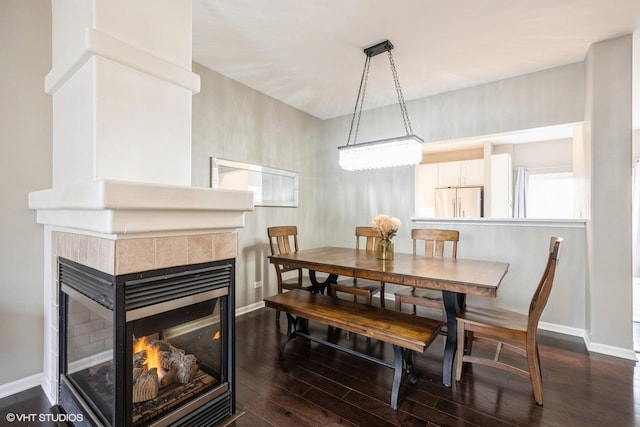 dining room featuring dark wood-style floors, a tile fireplace, and baseboards