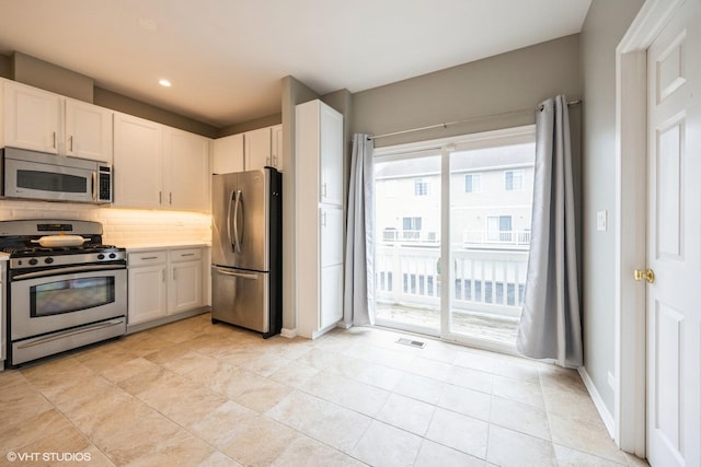 kitchen with stainless steel appliances, visible vents, white cabinets, light countertops, and backsplash