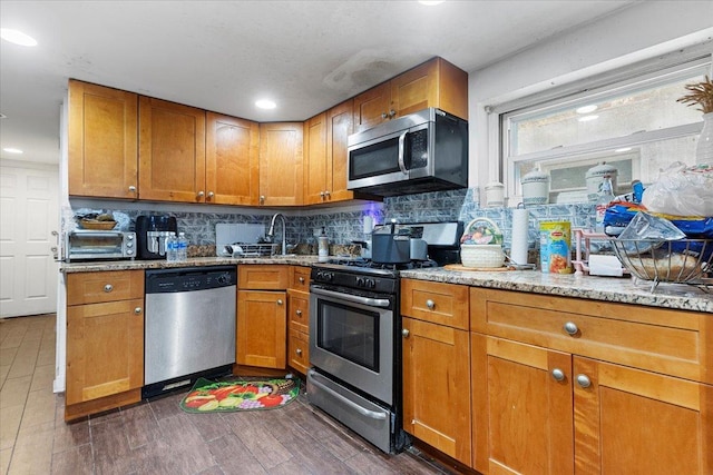 kitchen featuring stainless steel appliances, light stone counters, brown cabinets, and decorative backsplash