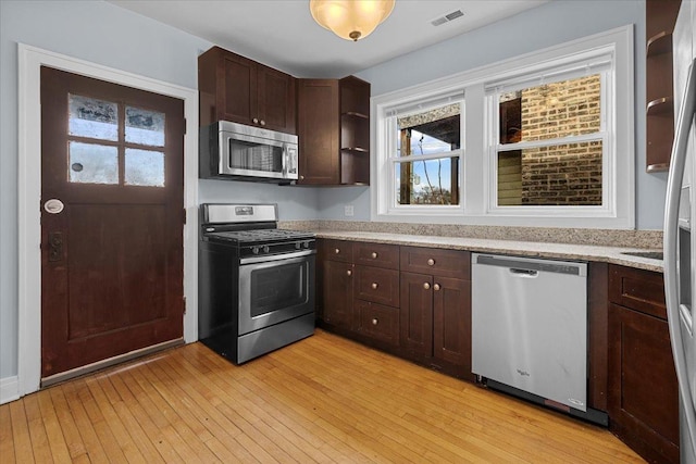 kitchen with appliances with stainless steel finishes, light wood-type flooring, visible vents, and dark brown cabinetry