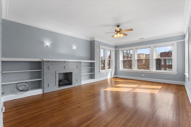 unfurnished living room featuring baseboards, hardwood / wood-style floors, crown molding, a brick fireplace, and built in shelves