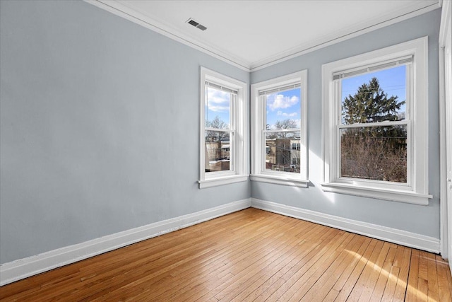 empty room featuring ornamental molding, light wood-style floors, visible vents, and baseboards