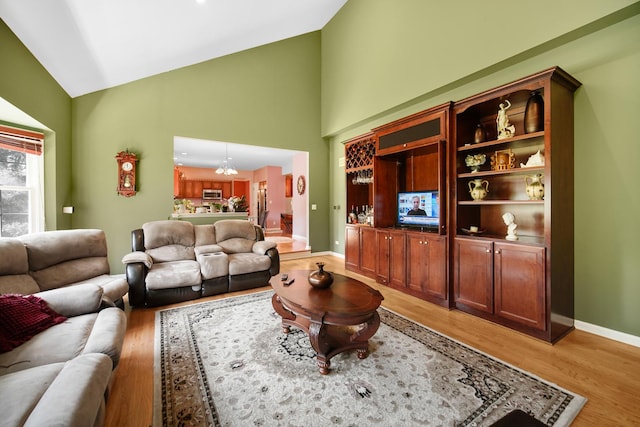 living area with high vaulted ceiling, light wood-type flooring, an inviting chandelier, and baseboards