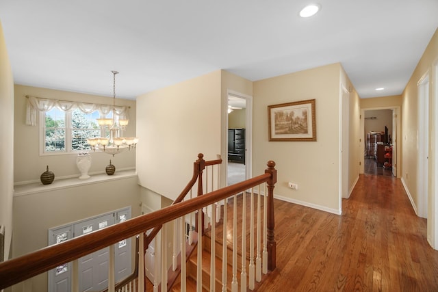 corridor with recessed lighting, a notable chandelier, wood finished floors, an upstairs landing, and baseboards