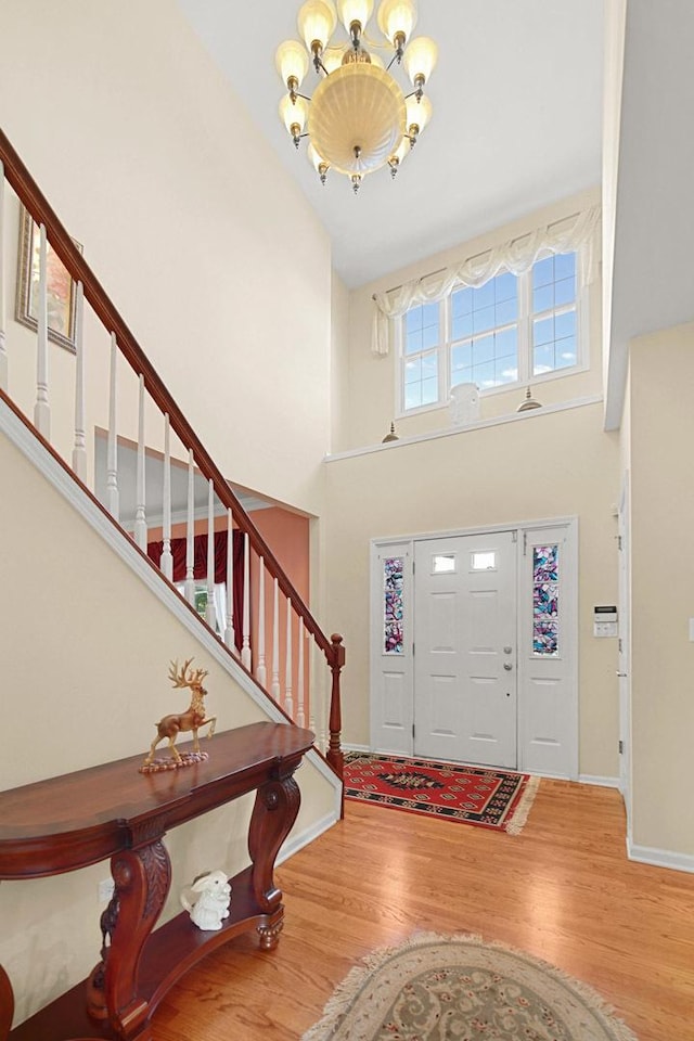 foyer featuring a towering ceiling, an inviting chandelier, wood finished floors, baseboards, and stairs