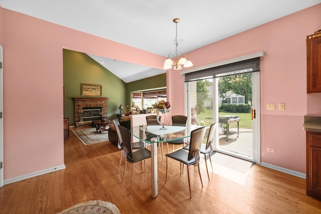 dining space featuring lofted ceiling, light wood-style flooring, an inviting chandelier, a glass covered fireplace, and baseboards