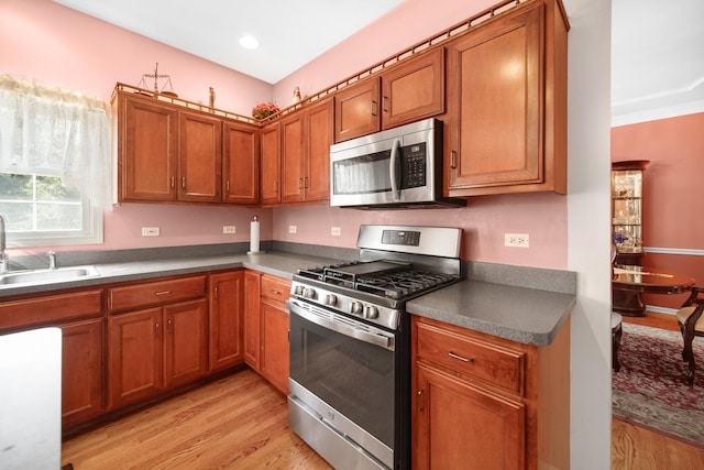 kitchen featuring recessed lighting, stainless steel appliances, a sink, light wood finished floors, and brown cabinetry