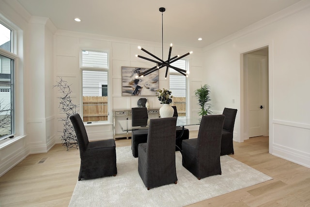 dining area with visible vents, crown molding, light wood-type flooring, a decorative wall, and a notable chandelier