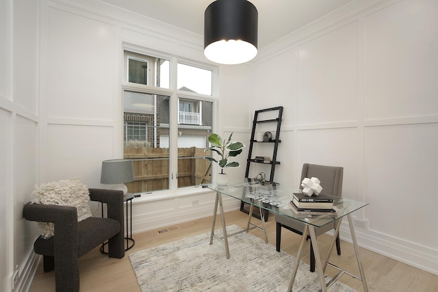 office with light wood-style floors, visible vents, a decorative wall, and crown molding