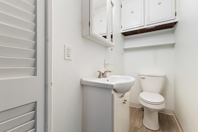 half bath featuring a sink, baseboards, toilet, and wood finished floors