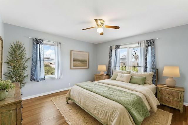 bedroom featuring ceiling fan, baseboards, multiple windows, and wood finished floors