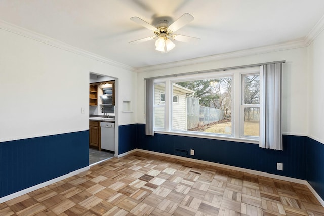 empty room featuring baseboards, wainscoting, a ceiling fan, and crown molding