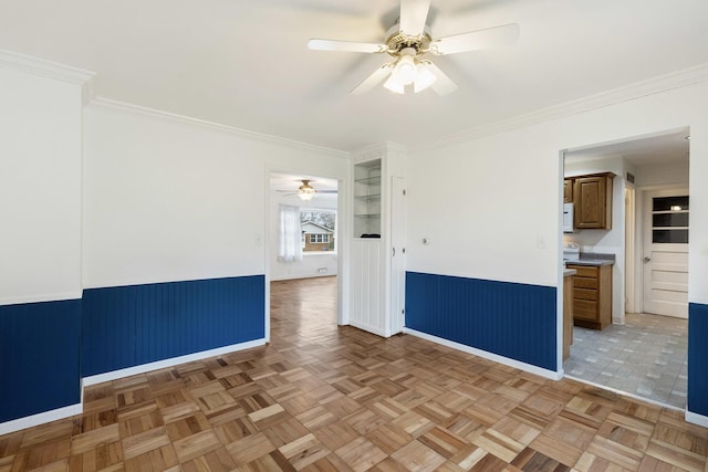 empty room with a wainscoted wall, a ceiling fan, and crown molding