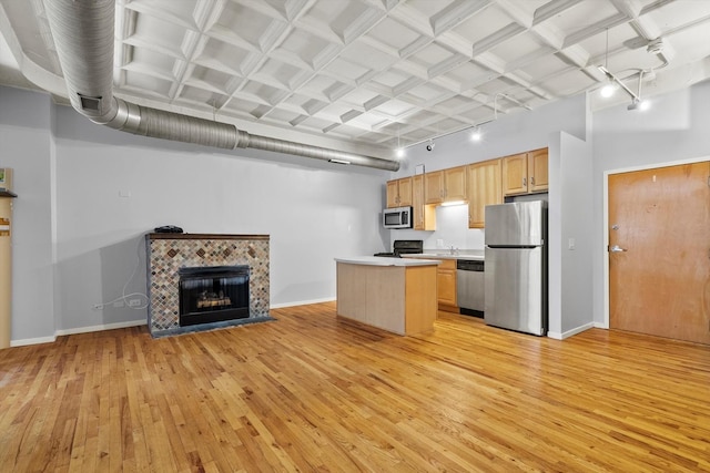 kitchen featuring light wood finished floors, baseboards, a tile fireplace, stainless steel appliances, and light brown cabinets