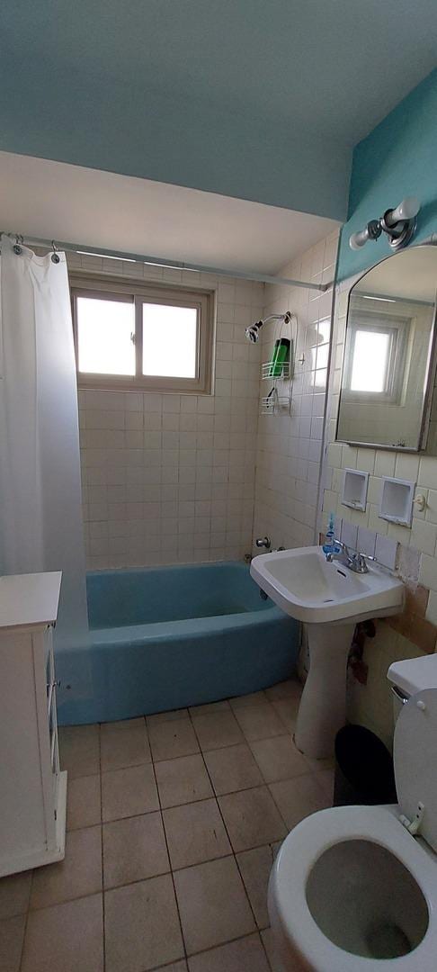 bathroom featuring tile walls, shower / bath combination with curtain, decorative backsplash, toilet, and tile patterned flooring