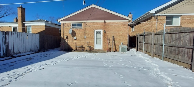 snow covered house featuring brick siding, central AC unit, and fence