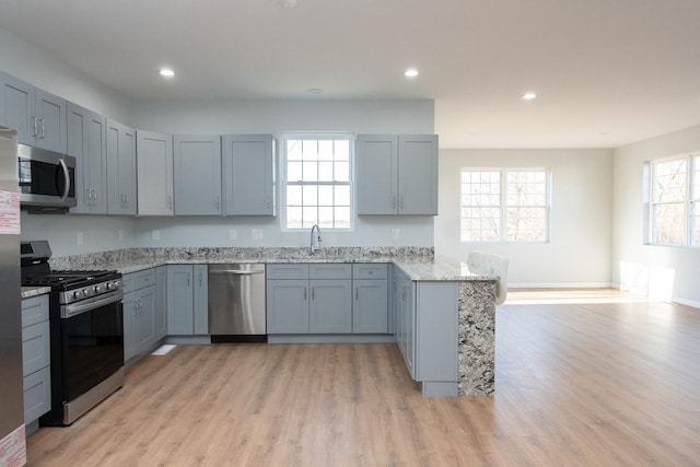 kitchen featuring recessed lighting, light wood-style flooring, appliances with stainless steel finishes, light stone countertops, and a peninsula