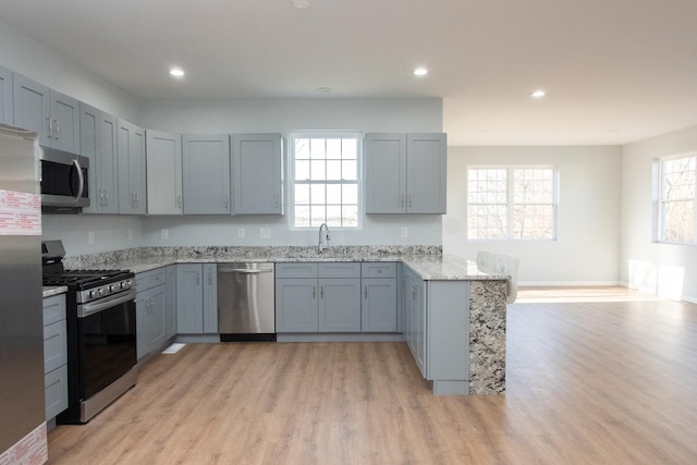 kitchen with light wood-style flooring, light stone counters, a peninsula, stainless steel appliances, and a sink