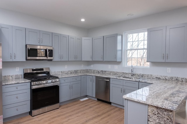 kitchen with light wood-style flooring, appliances with stainless steel finishes, a peninsula, gray cabinets, and a sink