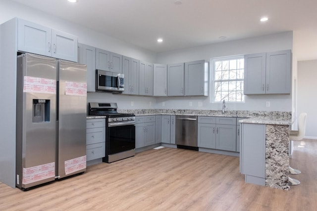 kitchen with light stone counters, stainless steel appliances, gray cabinetry, light wood-style floors, and recessed lighting