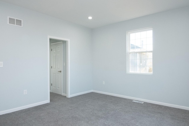 spare room featuring visible vents, dark carpet, and baseboards