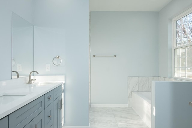 bathroom with marble finish floor, double vanity, a sink, a tub, and baseboards