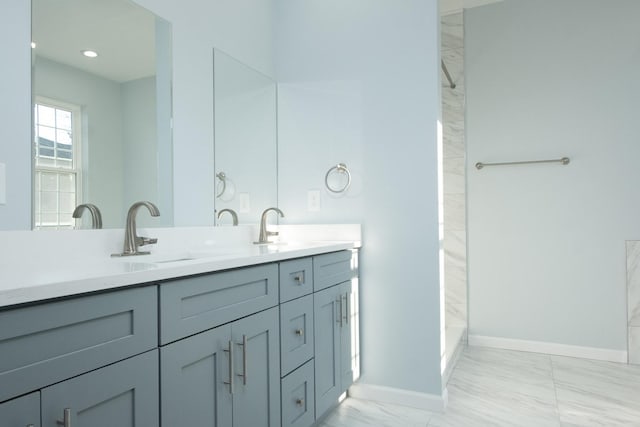 bathroom with marble finish floor, double vanity, a sink, and baseboards