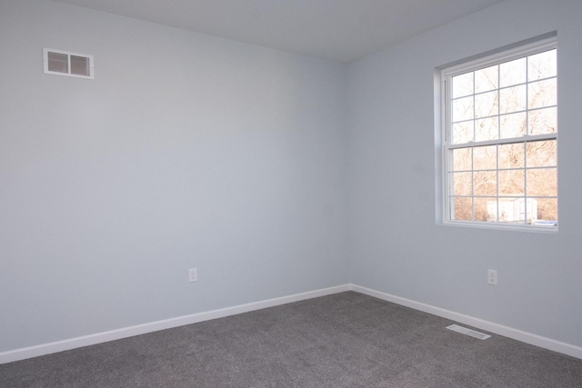 unfurnished room with dark colored carpet, visible vents, and baseboards