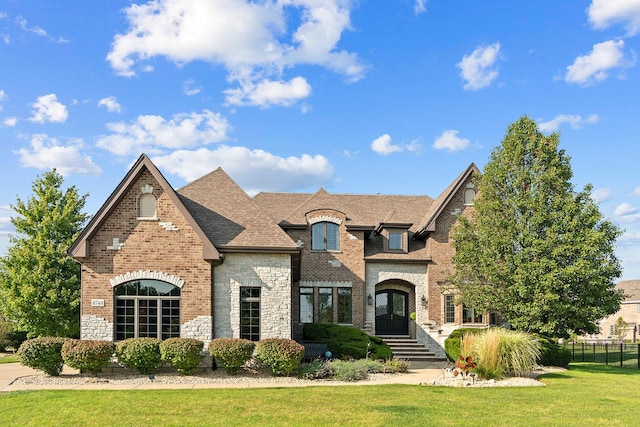 french country inspired facade with french doors, brick siding, a shingled roof, fence, and a front lawn