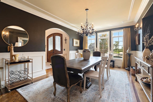 dining room with arched walkways, a wainscoted wall, wood finished floors, french doors, and ornamental molding