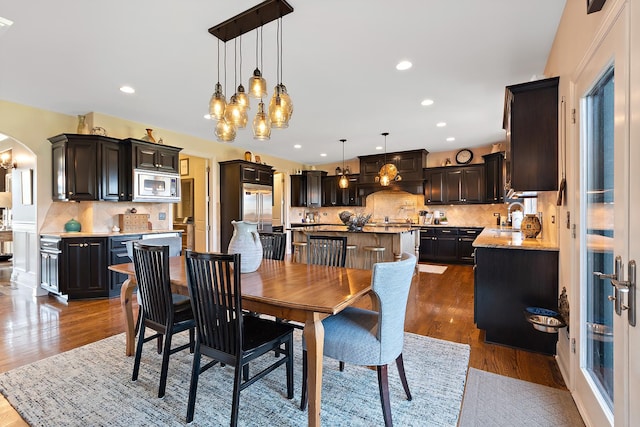 dining space featuring arched walkways, dark wood finished floors, and recessed lighting