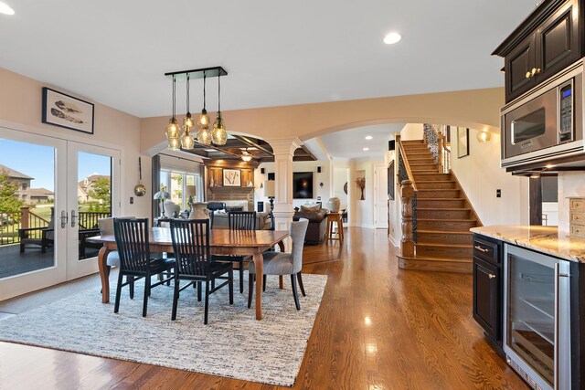 dining area with wine cooler, wood finished floors, stairs, french doors, and ornate columns