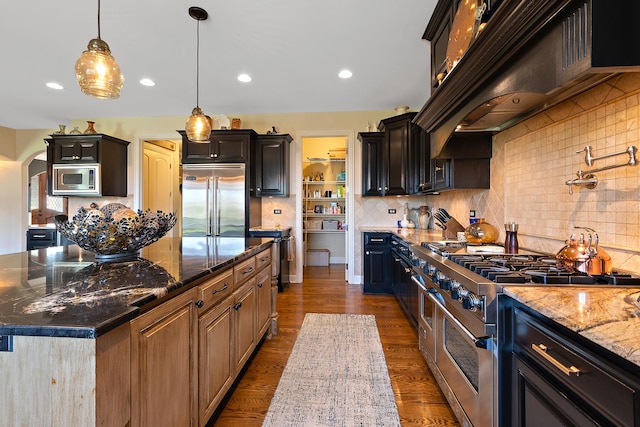 kitchen featuring arched walkways, dark stone counters, dark wood-style floors, built in appliances, and under cabinet range hood