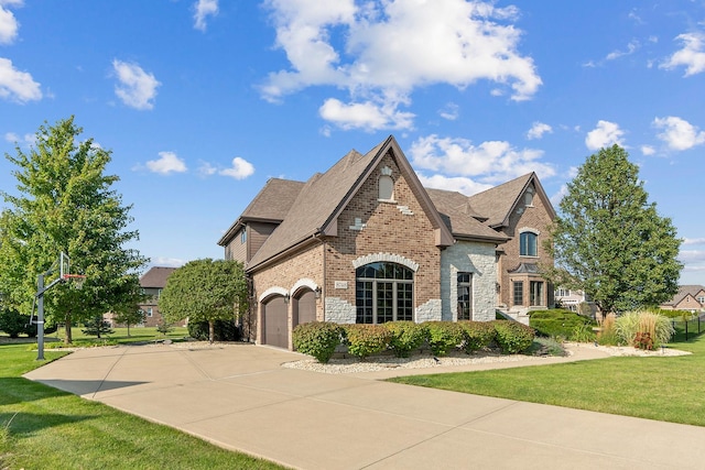 french country inspired facade featuring brick siding, roof with shingles, a front yard, a garage, and driveway