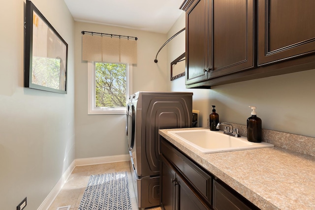 clothes washing area featuring light tile patterned flooring, washing machine and dryer, a sink, baseboards, and cabinet space