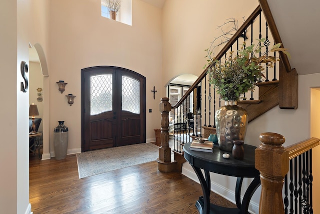 entrance foyer with stairs, arched walkways, french doors, and wood finished floors