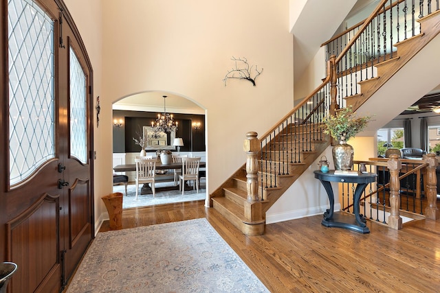 entrance foyer with arched walkways, a notable chandelier, a high ceiling, wood finished floors, and stairs