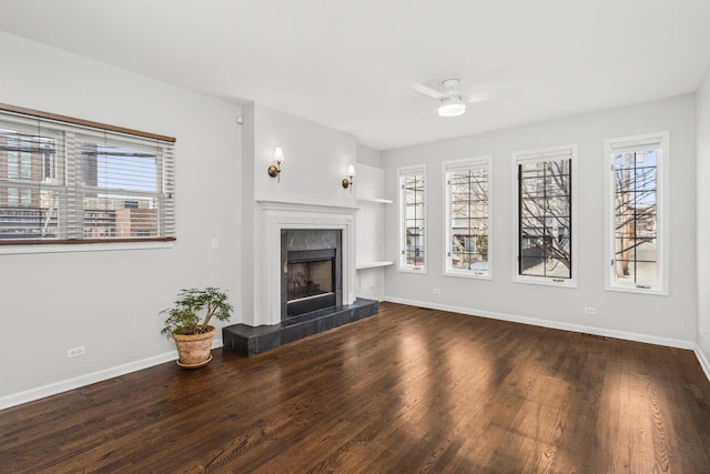 unfurnished living room with a ceiling fan, baseboards, a tiled fireplace, and wood finished floors