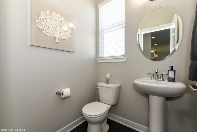 half bathroom featuring a sink, wood finished floors, toilet, and baseboards