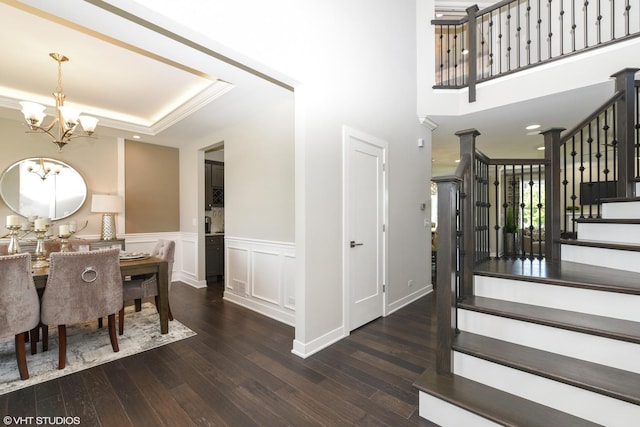 dining area with a raised ceiling, wainscoting, wood finished floors, a chandelier, and stairs