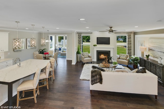 living room featuring recessed lighting, a fireplace with flush hearth, a ceiling fan, ornamental molding, and dark wood-style floors