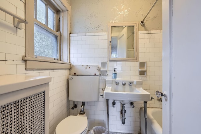 bathroom with a wainscoted wall, tile walls, toilet, a sink, and wallpapered walls