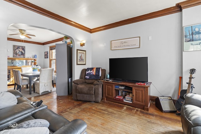 living area with arched walkways, ornamental molding, wood-type flooring, and a ceiling fan