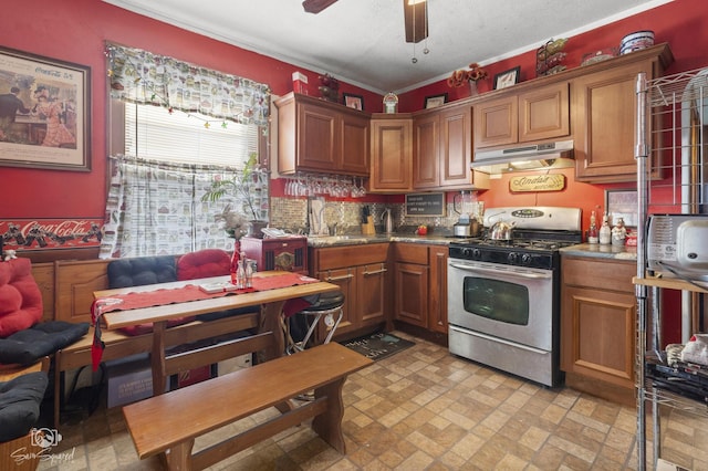 kitchen with ceiling fan, under cabinet range hood, stainless steel gas range, tasteful backsplash, and brown cabinetry