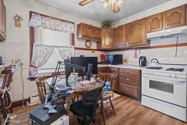 kitchen with light wood-style flooring, under cabinet range hood, light countertops, white gas range oven, and brown cabinetry